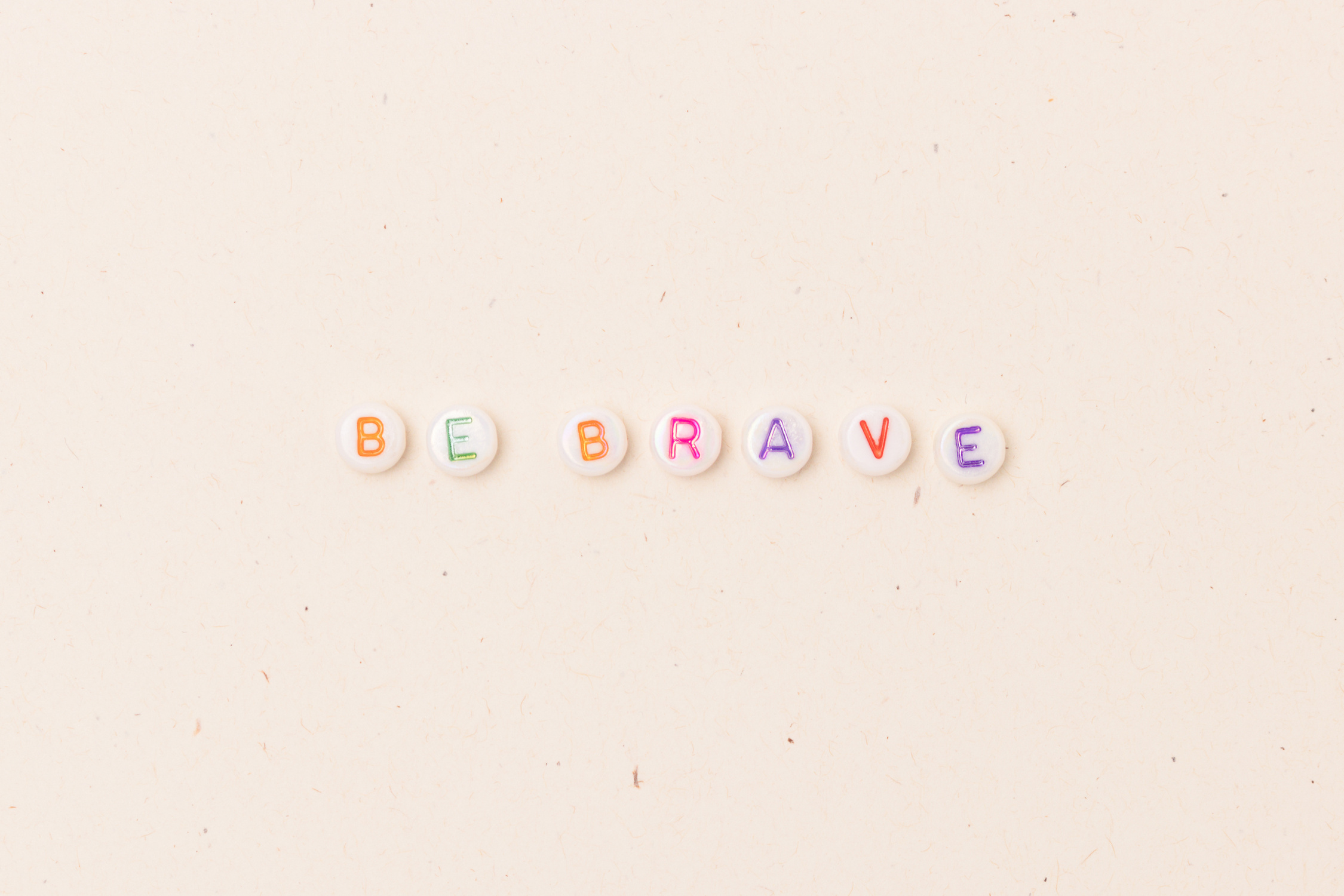 Be brave. Quote made of white round beads with multicolored letters.